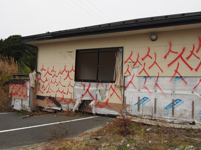 富岡駅前。津波で流された家が道路の上に。無数の「人」の落書きがそこら中に書かれている。